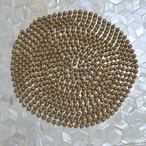 May include: A decorative square tray with a mother-of-pearl geometric pattern and a central circle of small, gold-colored beads. The tray has a raised edge and is set on a wooden surface.