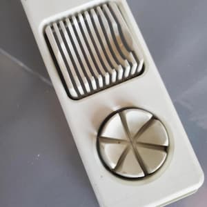 May include: A white plastic egg slicer with a hinged top and a circular cutting section. The slicer has parallel wires for slicing and a star-shaped section for wedges. The item is designed for kitchen use.