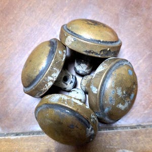 May include: A collection of five antique brass door knobs. The knobs have a rounded, oval shape with a dark rim and a tarnished, aged appearance. The brass has a warm, golden hue with signs of wear.