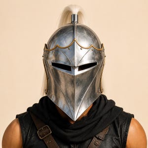 May include: A polished silver metal helmet featuring a pointed visor, gold-toned trim along the edges, and a long white plume extending from the top. The helmet is worn over a black sleeveless garment with brown leather straps and a buckle.
