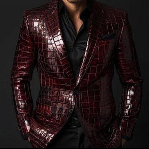 Peut inclure: Un blazer bordeaux profond doté d'une texture brillante en relief façon peau de crocodile. La veste présente un col structuré, des revers crantés et une fermeture à un bouton, portée sur une chemise noire unie à col pointu.