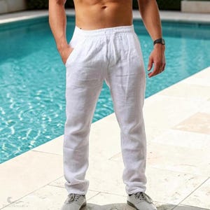 May include: A pair of white trousers featuring an elasticated waistband with a drawstring, two side pockets, and a straight-leg cut. The fabric has a visible woven texture, and the trousers are worn with grey lace-up trainers.