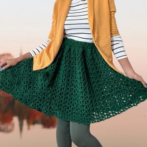 May include: A green crochet skirt with a flared silhouette. The skirt is worn with a white and black striped turtleneck shirt and a mustard yellow blazer.