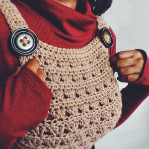 May include: A brown crocheted top with a unique design. The top features two large, round buttons with a floral design.