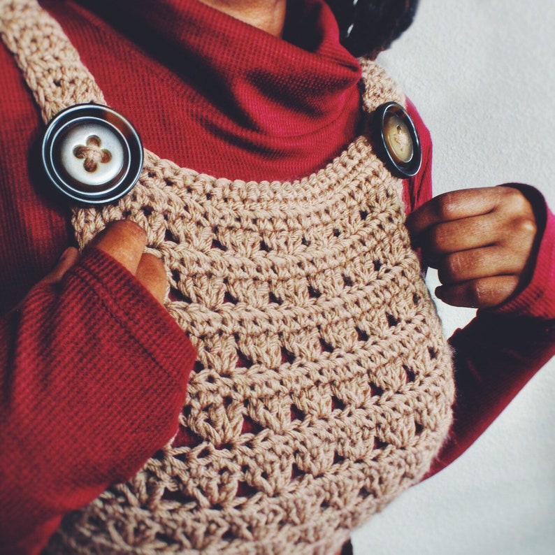 May include: A brown crocheted top with a unique design. The top features two large, round buttons with a floral design.