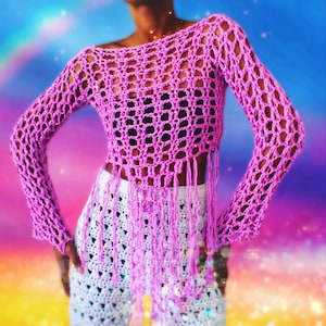 May include: A pink crochet top with long sleeves and a fringe hem. The top is made with a loose, open stitch pattern.