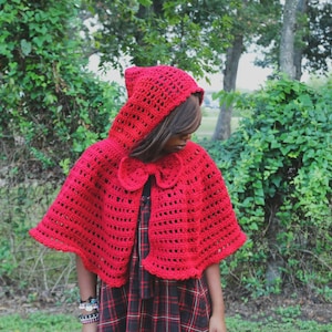 May include: A red crocheted hooded cape with a bow at the neck. The cape is made with a lacy stitch and has a wide, flowing hood.