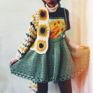 K&ouml;nnte beinhalten: Ein gr&uuml;ner H&auml;kelrock mit einer wei&szlig;en und gelben H&auml;keljacke mit Sonnenblumenmuster. Die Jacke hat eine braune Mitte in jeder Sonnenblume. Die Person tr&auml;gt ein schwarzes T-Shirt mit dem Text "Vincent Van Gogh" und einem Sonnenblumenbild.