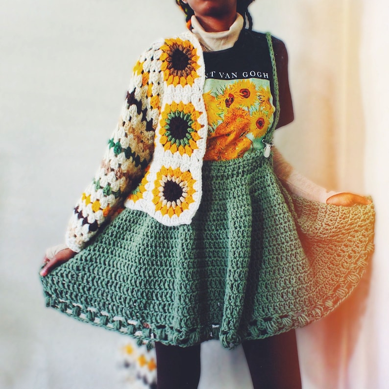 K&ouml;nnte beinhalten: Ein gr&uuml;ner H&auml;kelrock mit einer wei&szlig;en und gelben H&auml;keljacke mit Sonnenblumenmuster. Die Jacke hat eine braune Mitte in jeder Sonnenblume. Die Person tr&auml;gt ein schwarzes T-Shirt mit dem Text "Vincent Van Gogh" und einem Sonnenblumenbild.