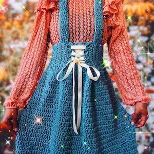 May include: A teal crochet skirt with a white ribbon and a lace-up detail at the waist. The skirt is worn over a peach-colored lace top with ruffled sleeves.