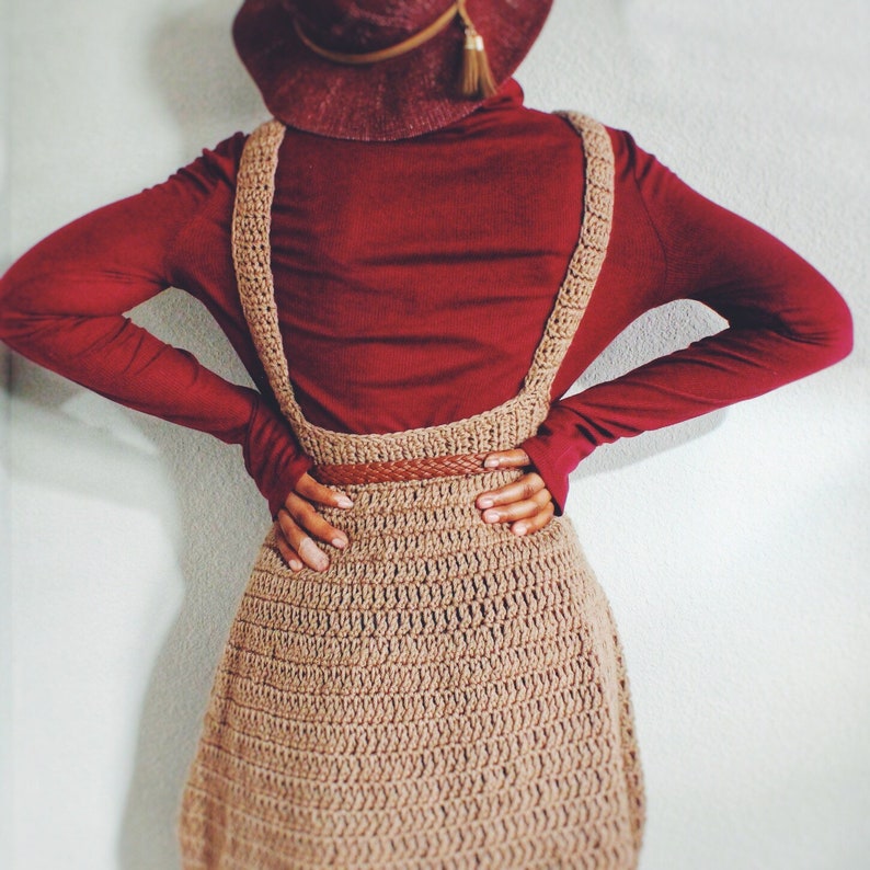 May include: A brown crocheted dress with straps over a burgundy turtleneck sweater. The dress has a crocheted belt.