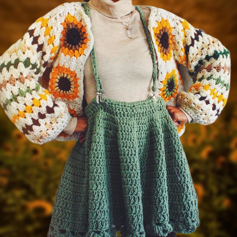 K&ouml;nnte beinhalten: Ein gr&uuml;ner H&auml;kelrock mit einer wei&szlig;en H&auml;keljacke mit Sonnenblumenmuster. Die Jacke hat eine braune, gelbe und gr&uuml;ne Farbgebung.