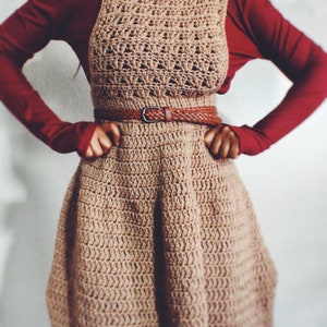 May include: A brown crocheted dress with a brown leather belt. The dress has a flared skirt and a fitted bodice.