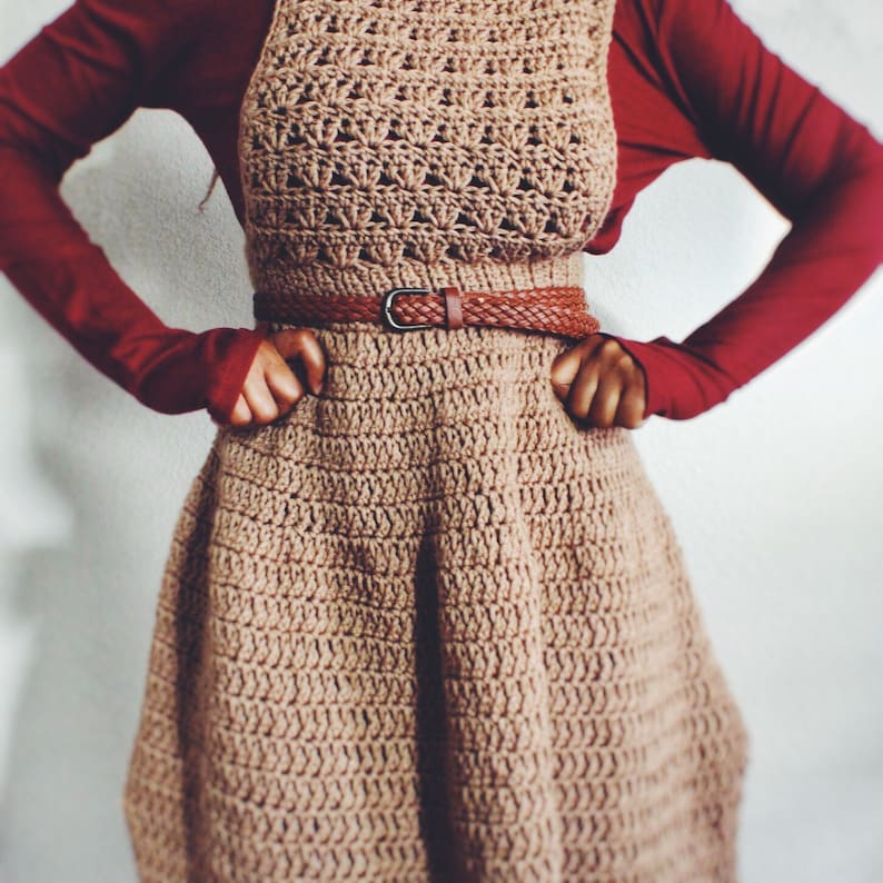 May include: A brown crocheted dress with a brown leather belt. The dress has a flared skirt and a fitted bodice.
