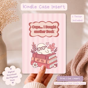 Könnte beinhalten: Ein rechteckiger Kindle-Hülleneinsatz mit hellrosa gestreiftem Hintergrund. Der Text "Oops... I Bought another Book" steht in einem gewellten Rahmen. Darunter ruht ein weißes Gespenst mit herzförmiger Brille auf drei gestapelten Büchern.