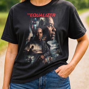 May include: A black short-sleeved t-shirt featuring a graphic print of the movie The Equalizer. The design includes the red text THE EQUALIZER at the top, with a collage of scenes and character portraits from the film in shades of black and gray.