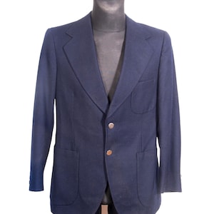 Könnte beinhalten: Ein marineblauer Blazer mit zwei Vordertaschen und zwei goldfarbenen Knöpfen. Der Blazer wird auf einer schwarzen Schaufensterpuppe präsentiert. Die Jacke hat ein klassisches Design mit fallenden Revers und einer taillierten Passform. Der Stoff scheint eine Wollmischung zu sein.