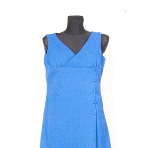 Puede incluir: Un vestido azul sin mangas con escote en V y un patrón ondulado texturizado en toda la tela. La prenda incluye un detalle de panel lateral adornado con cinco botones azules a juego que corren verticalmente por el lado izquierdo del corpiño.