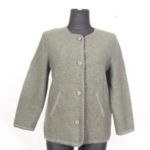 Puede incluir: Chaqueta verde salvia con cuello redondo y tres botones decorativos. La chaqueta tiene dos bolsillos delanteros y un ribete festoneado a lo largo de los bordes. Las mangas son largas y la tela parece ser un tejido de punto texturizado.