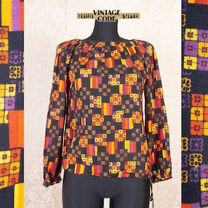 May include: A long-sleeved blouse with a black background and a repeating geometric pattern in orange, yellow, and purple. The blouse has a round neckline and gathered cuffs. The text "VINTAGE CODE" is visible at the top.