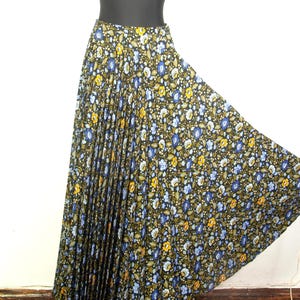May include: A long, pleated skirt with a floral pattern. The skirt features a black background with blue, yellow, and white flowers. The skirt is displayed on a mannequin.
