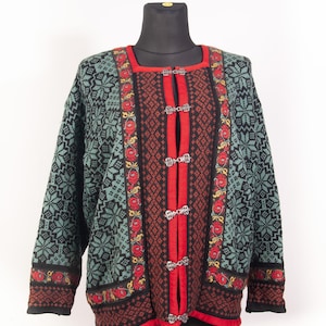 Può includere: Un maglione vintage a maniche lunghe con un motivo dettagliato. Il maglione presenta una base nera con disegni a fiocco di neve verde acqua sulle maniche e sulla parte superiore del corpo. La parte anteriore ha un pannello rosso con chiusure argentate e accenti floreali. Il bordo è rosso.