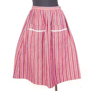 May include: A knee-length skirt featuring a vertical striped pattern in shades of red, white, and blue. The skirt has a gathered waistband and two front patch pockets, each accented with a decorative white scalloped trim along the top edge.