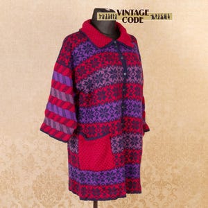 Könnte beinhalten: Ein Vintage-Mantel in Rot, Lila und Marineblau. Der Mantel hat ein Schneeflockenmuster, gestreifte Ärmel und zwei Vordertaschen. Der Kragen und die Knöpfe sind marineblau. Der Text "VINTAGE CODE" ist oben aufgedruckt.