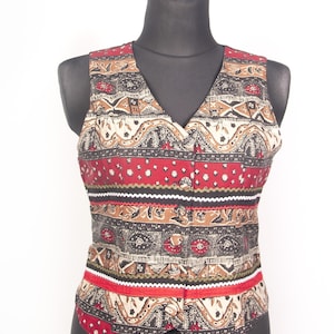 Puede incluir: Un chaleco sin mangas con escote en V y cierre de botones en la parte delantera. La prenda está decorada con un diseño de patrón horizontal en tonos rojo, negro, beige y blanco, que incorpora formas geométricas, motivos florales y líneas onduladas.