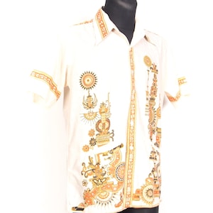 May include: Cream-coloured button-down shirt with short sleeves. The shirt features intricate orange and gold geometric patterns and designs on the front, sleeves, and collar. The shirt is displayed on a black mannequin.