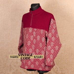 May include: A burgundy and white patterned sweater with a high collar and a quarter-zip closure. The sweater features a diamond pattern on the sleeves and lower body. The text "VINTAGE CODE" is visible on the lower left.