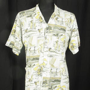 May include: Short-sleeved shirt in white, patterned with golf scenes. The design includes golfers, umbrellas, and golf course elements in yellow, green, and brown. The shirt has a V-neck collar.