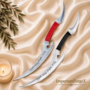 May include: Two curved metal daggers with pointed tips and notched blades. One dagger features a red wrapped handle, while the other has a black wrapped handle. Both blades are engraved with flowing script text along the curved edge.