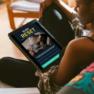 以下が含まれることがあります： SLEEP RESETというタイトルのドキュメントを表示するデジタルタブレット。カバーには、アイマスクをしてベッドで眠る人物の写真が掲載されています。画面上のテキストには、The complete guide to falling asleep faster, staying asleep, and waking up restoredと記載されています。