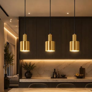 May include: A linear pendant light fitting featuring three cylindrical brass-toned metal shades suspended by black cords from a rectangular brass-toned ceiling canopy. Each shade emits a warm downward light, creating a focused illumination.