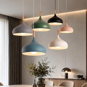 May include: A collection of six dome-shaped pendant lights suspended at varying heights. Each lamp features a smooth matte finish in gray, green, black, pink, blue, or white, with a light-colored wooden connector at the top and a white interior.