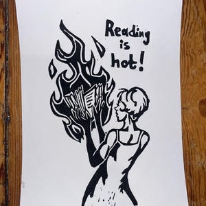 Könnte beinhalten: Ein schwarz-weißer Linoldruck auf Papier, der eine Figur zeigt, die ein von stilisierten Flammen umgebenes Buch hält. Der Text "Reading is hot!" ist in schwarzer Tinte über der Figur gedruckt. Das Bild verwendet kontrastreiche Linien.