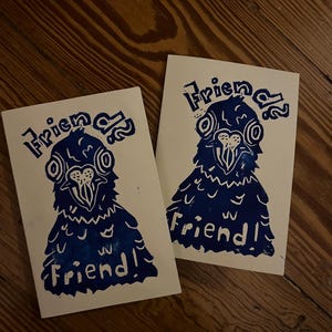 Puede incluir: Dos tarjetas rectangulares blancas con una ilustración en bloque de color azul oscuro de un pájaro con ojos grandes y pico. El texto "Friend" está impreso en azul oscuro encima y debajo de la ilustración del pájaro en ambas tarjetas.