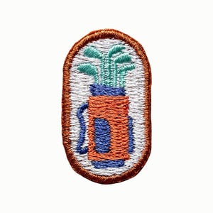 May include: An oval-shaped embroidered patch featuring a golf bag with clubs in shades of orange, blue, and mint green against a white background, all enclosed within a thick, stitched copper-colored border with a textured thread finish.