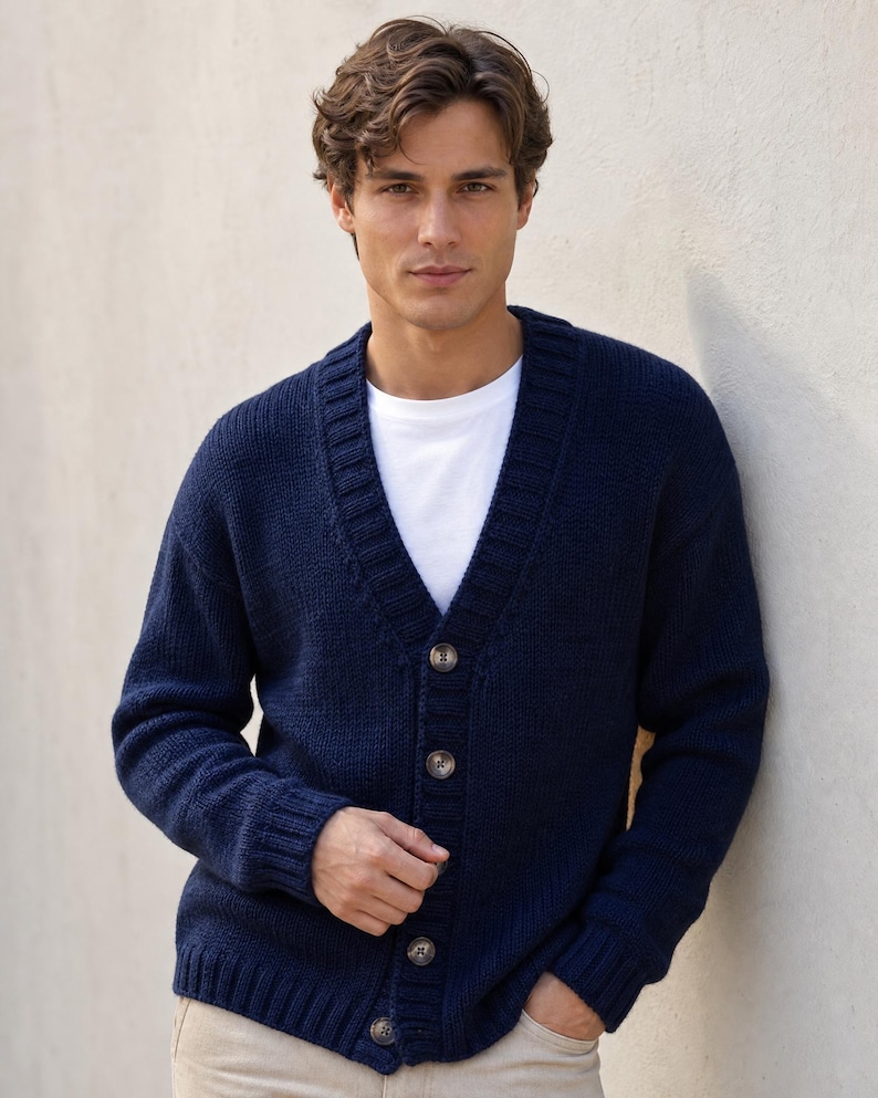 Op de afbeelding: Een marineblauw gebreid vest met lange mouwen, een V-hals, een knoopsluiting aan de voorzijde met vier zichtbare knopen en geribbelde details bij de kraag, manchetten en zoom, gedragen over een effen wit T-shirt met ronde hals.