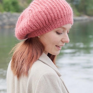 Peut inclure: Un béret en tricot rose poudré doux présentant une texture côtelée verticale prononcée. Le bonnet est confectionné dans un fil duveteux et texturé, avec une silhouette arrondie et légèrement affaissée qui repose sur un bord ajusté.