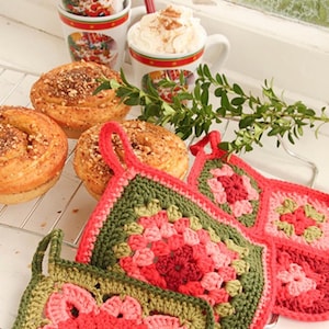 Puede incluir: Tres agarraderas cuadradas de ganchillo con patrones de granny square inspirados en flores en tonos verde oliva, rosa brillante y rojo intenso. Cada agarradera incluye un pequeño lazo para colgar, hecho con hilo en un diseño de punto texturizado.