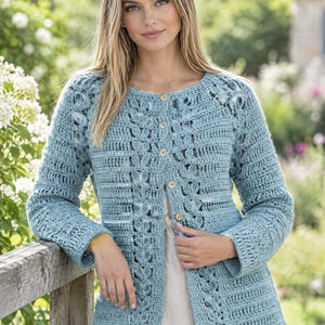 May include: A light blue long-sleeve cardigan featuring a textured crochet pattern with vertical leaf-like motifs. The garment has a round neckline and a front button closure with five small, round, light-colored wooden buttons down the center.