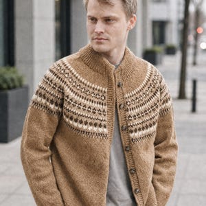 Könnte beinhalten: Eine beigefarbene Strickjacke mit einer runden Passe, die ein geometrisches Muster in Dunkelbraun und Creme aufweist. Das Kleidungsstück hat einen gerippten Kragen, Bündchen und Saum sowie eine vertikale Reihe dunkler Knöpfe an der Vorderseite.