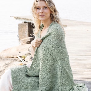 May include: A sage green rectangular blanket featuring a complex, repeating geometric crochet pattern with textured stitches. The textile is crafted from yarn in a soft, muted green hue, showcasing a detailed, interconnected square motif design.