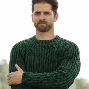 Peut inclure: Un pull à manches longues vert forêt foncé présentant une texture en tricot côtelé vertical prononcé, une encolure ronde classique et des manches raglan. Le vêtement est confectionné avec un motif de fil épais et texturé.