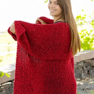 May include: A bright red, chunky knit cardigan featuring an open-front design with a loose, textured stitch pattern. The garment is crafted from thick yarn, creating a soft, voluminous appearance with long sleeves and a relaxed, draped silhouette.