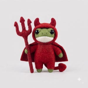 Peut inclure: Une figurine de grenouille verte en laine feutrée portant un costume de diable rouge à capuche avec des cornes et une cape. La grenouille tient une fourche rouge à trois dents et possède une petite queue rouge en forme de cœur.