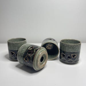 Puede incluir: Cuatro tazas de cerámica con un diseño bicolor que presenta un esmalte craquelado verde claro en la parte superior y un esmalte marrón oscuro brillante en la inferior. Cada taza incluye pequeños recortes en forma de corazón con borde dorado.