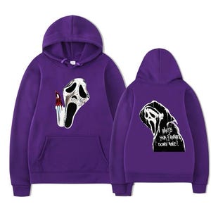 May include: A purple hooded sweatshirt featuring a graphic of a white ghost mask with a bloody knife on the front. The back displays a black and white illustration of a hooded figure with the text "What's your favourite scary movie?" in white.